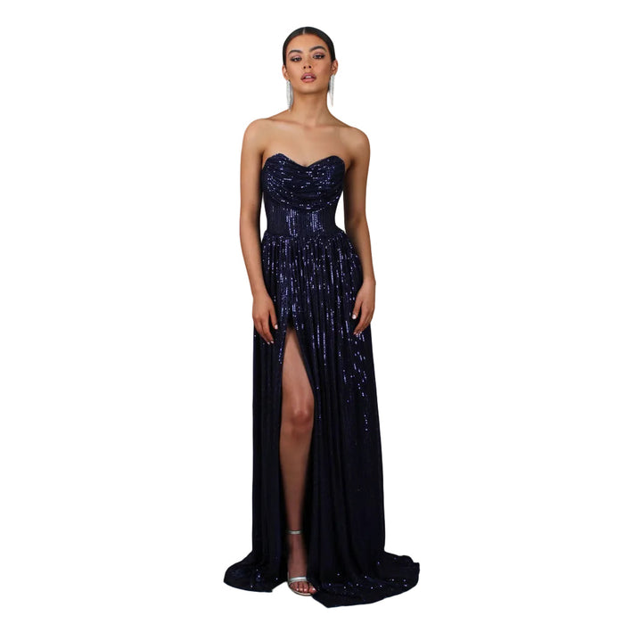 Woman wearing a strapless, sequined evening gown with a high slit on a gray background.