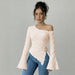Woman wearing a pink off-shoulder top with a belt and blue jeans on a gray background