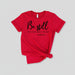 Red t-shirt with 'Be still and know that I am God' text on a wooden surface with shoes and jeans.