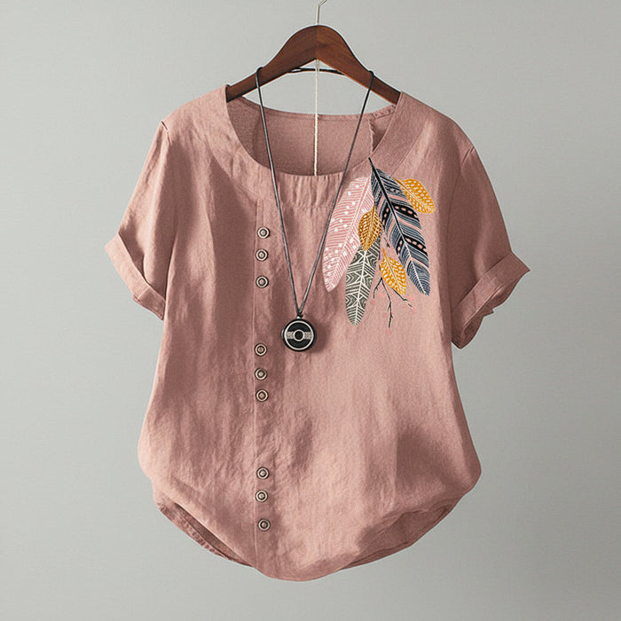 Pink blouse with feather design and buttons on a wooden hanger against a beige wall.
