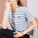Woman wearing a blue and white striped shirt with a small emblem, sitting on a couch.