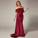 Woman in a burgundy evening gown standing against a dark background with a red couch.