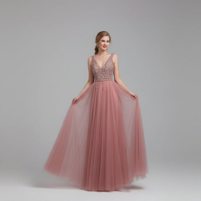 Pink evening gown with beaded top on a model against a white curtain background