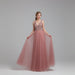 Pink evening gown with beaded top on a model against a white curtain background