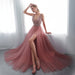 Woman in a pink evening gown with a high slit standing in a bright room.
